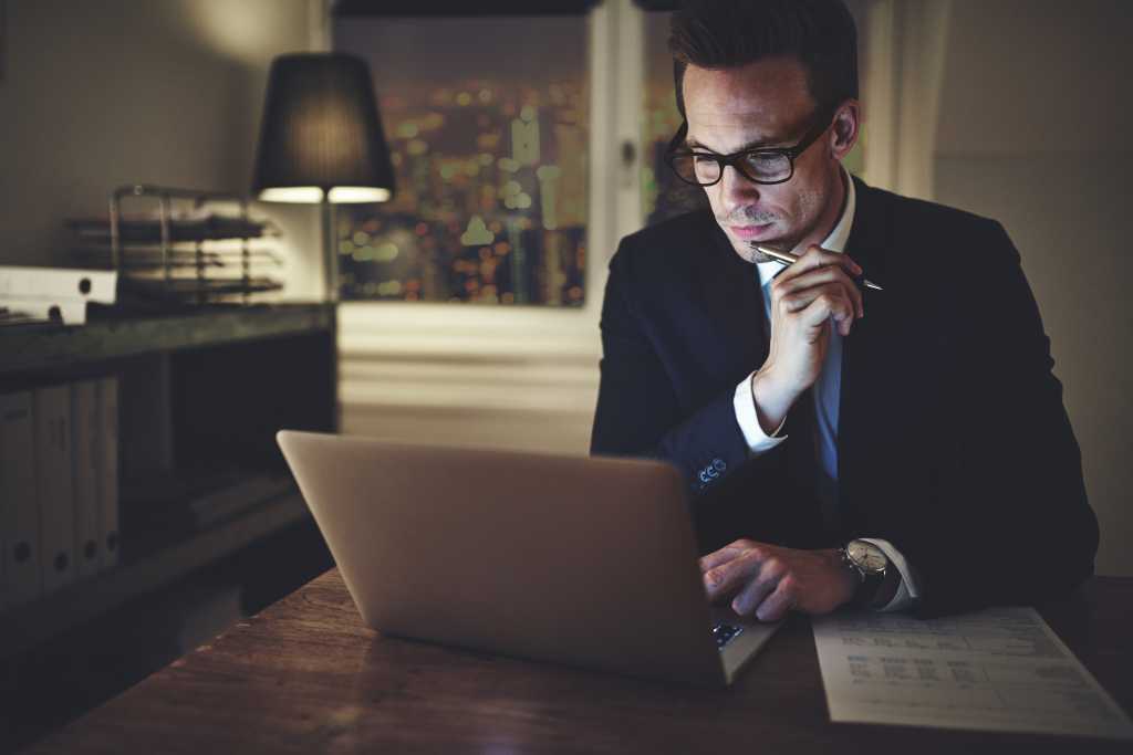 Serious businessman working on laptop at night sitting in office looking concentrated