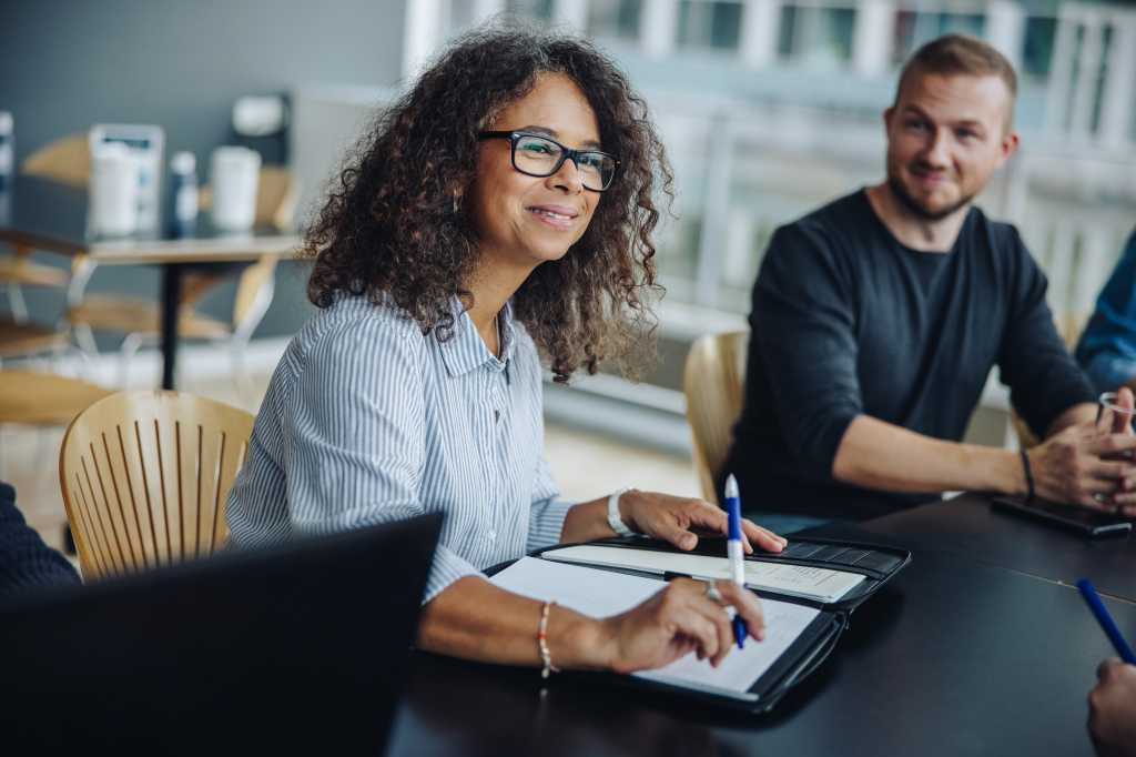 Mature businesswoman with a file sitting in meeting with her team. Female entrepreneur having meeting with colleagues in boardroom.