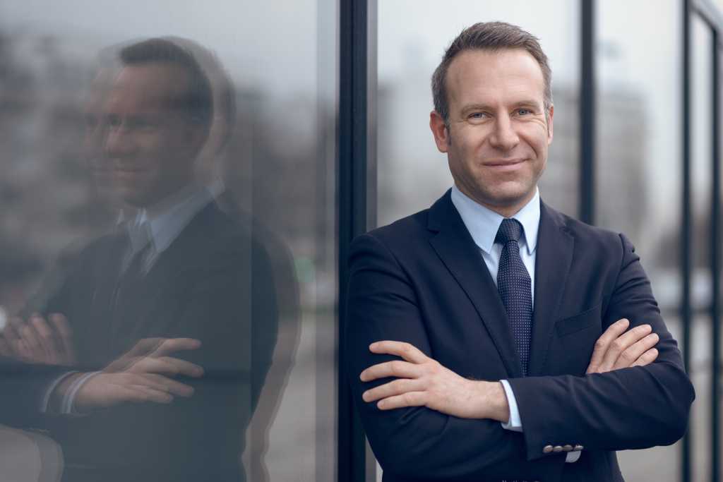 Single confident and handsome male businessman in blue suit and necktie with grin leaning on window outdoors