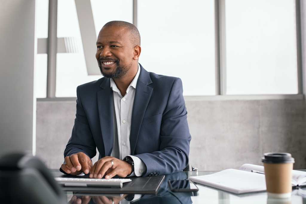 African american businessman working on his laptop. Mature business man in formal working at his desk. Smiling black middle aged man sitting in modern office working on computer and checking email.