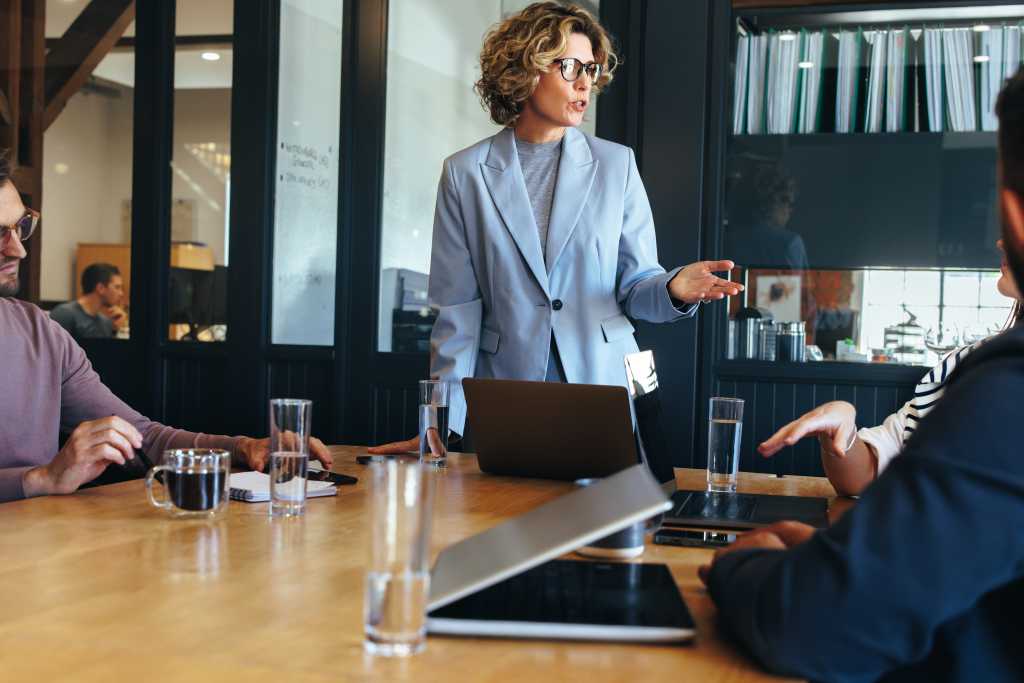 Business woman presenting an idea to her team in a meeting. Female manager having a discussion with her colleagues in a boardroom. Tech professionals working in an office.