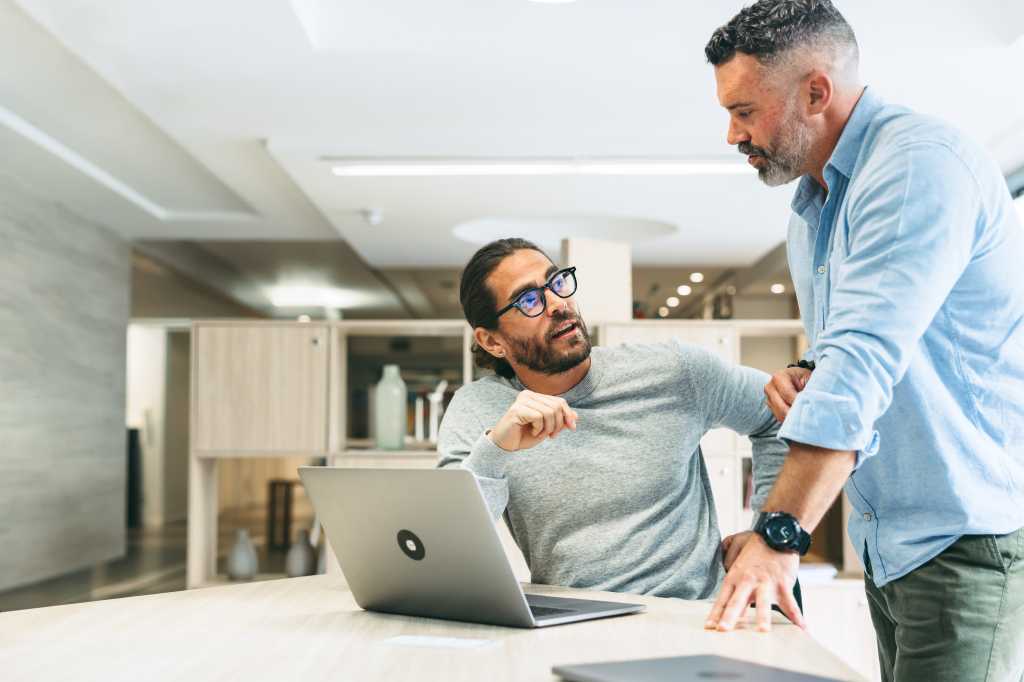 Two businessmen having a discussion while working together in a modern co-working office. Focused business professionals sharing ideas while planning a new project.