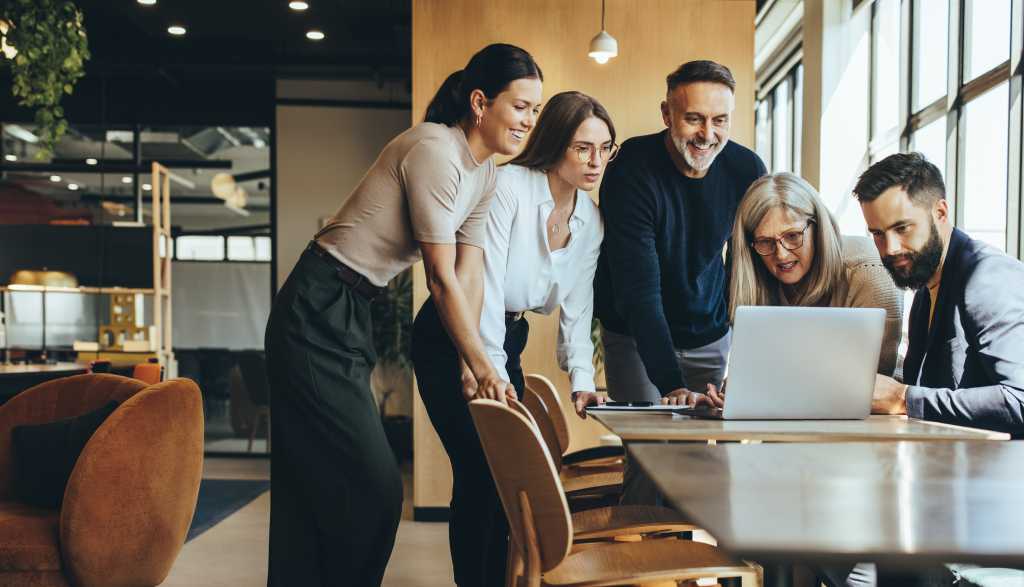Group of diverse businesspeople using a laptop while collaborating on a new project. Team of happy businesspeople looking at the laptop screen while working together in a modern workspace.