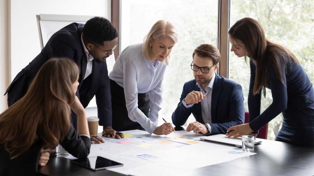 Serious senior mentor, corporate teacher training interns. Business coach, leader, boss teaching employees to analyze project documents, reviewing reports, using scrum method with sticky notes