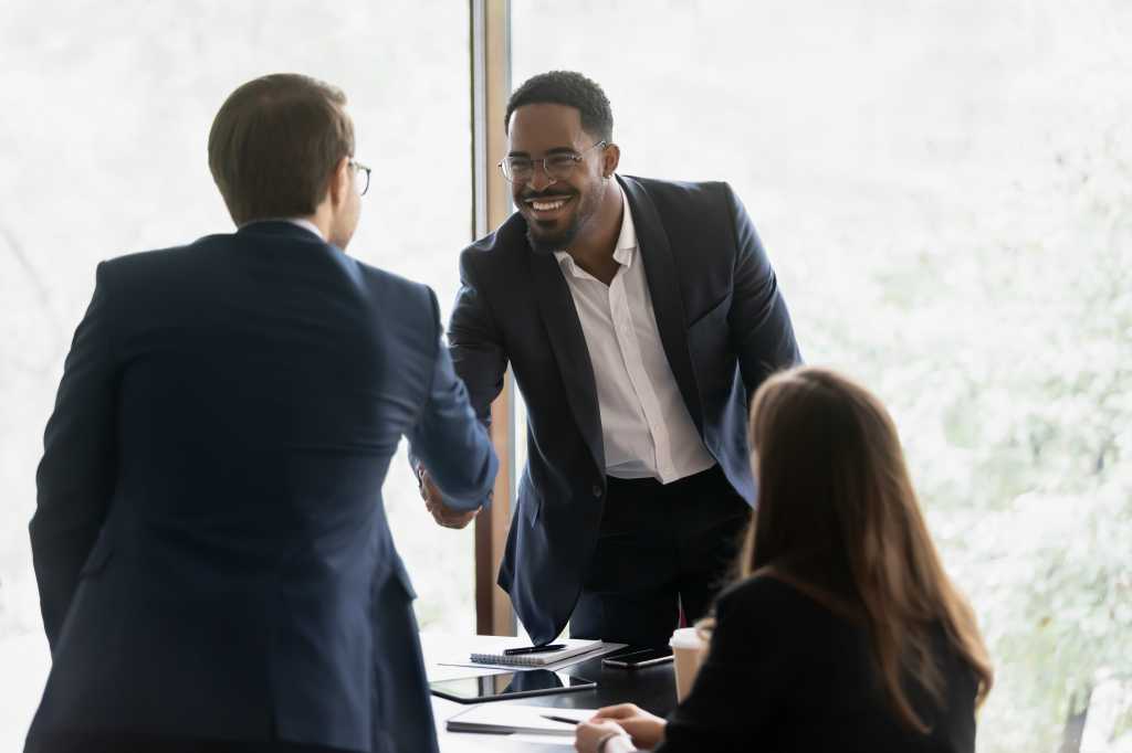 Smiling multiracial male business partners handshake greeting getting acquainted at office meeting, happy divers multiethnic man colleagues shake hands close deal or make agreement at briefing