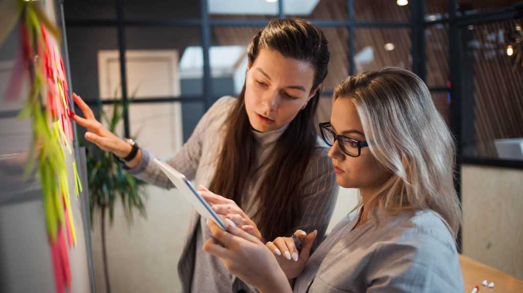 Teamwork, Projektmanagement, agile Methodik. Zwei junge Geschäftsfrauen im Büro arbeiten an einem Start-up. Kollegen planen Arbeiten und Entwicklungsstadien des Unternehmens, Kleberkleber-Blätter an Bord