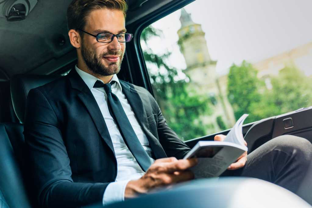 Young businessman sitting inside car and reading book