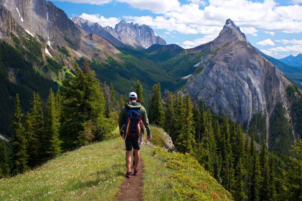 Healthy young man and a woman hiking and enjoying the view from the top of King Creek Ridge, Kananaskis Country, Alberta, Canada on a bright sunny day. Back packing in the Canadian Rockies.