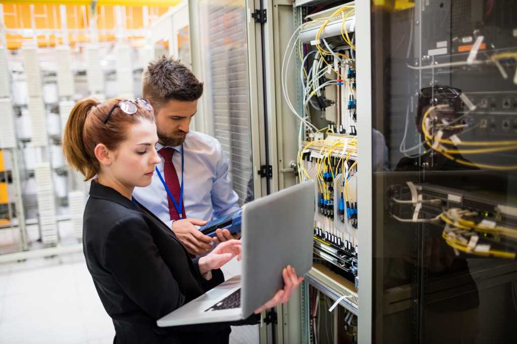 Technicians using laptop while analyzing server in server room