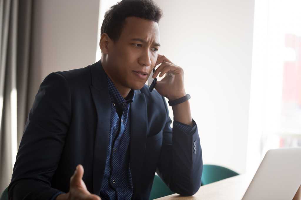 Angry stressed businessman disputing on phone with partner. Outraged african american manager, lawyer, banker, consultant or real estate agent listening bad news from client at office.