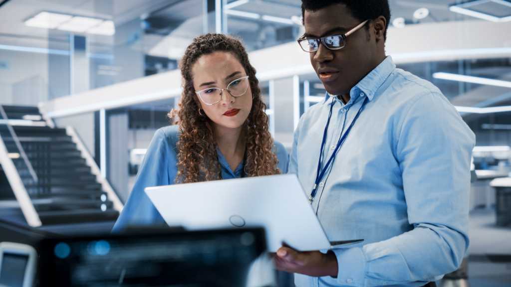 Portrait of Two Young Diverse Engineers Use Computer to Connect, Analyze and Discuss How to Program a Robot Dog. High Tech Research Laboratory with Modern Equipment.