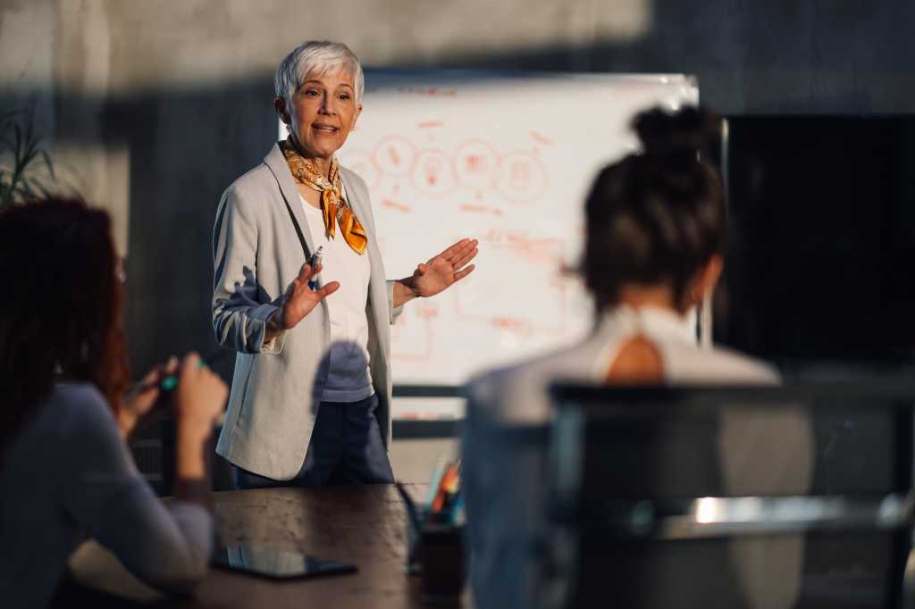 A mature female executive having presentation with her creative female team at corporate office. Senior businesswoman having briefing with with team of experts at boardroom and discussing project.