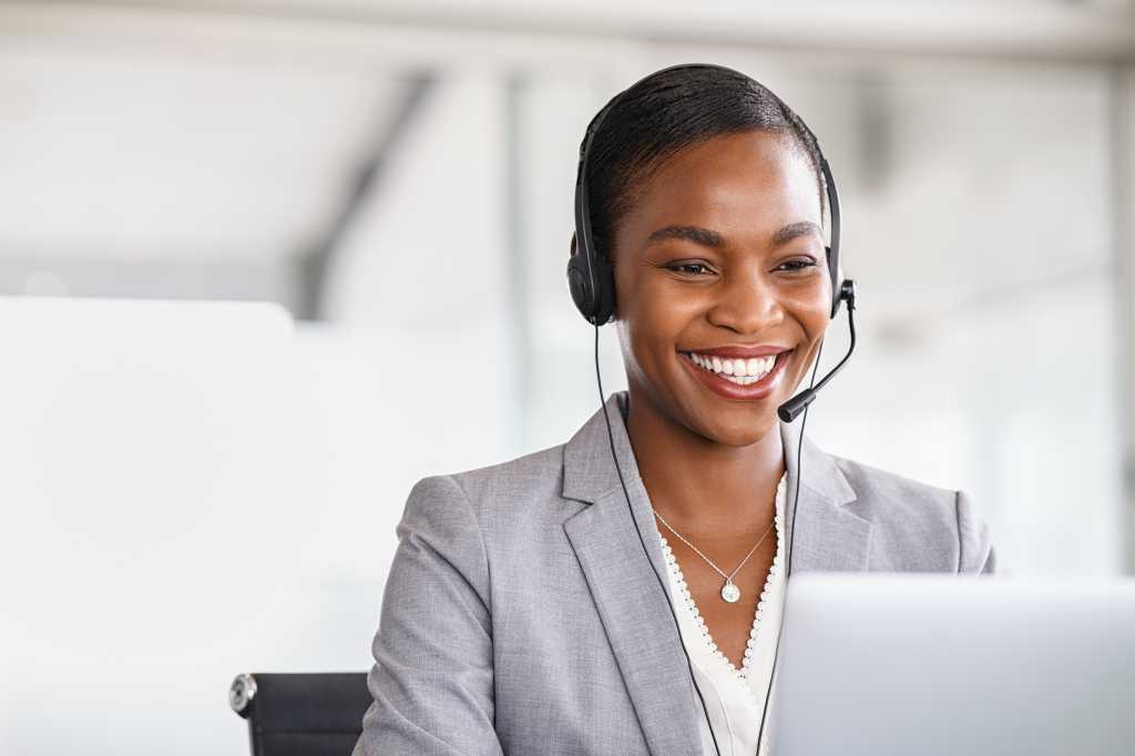 Smiling african american customer care representative working with headset in office. Black woman telemarketing agent working in call center. Call center agent with headset makinga video call.