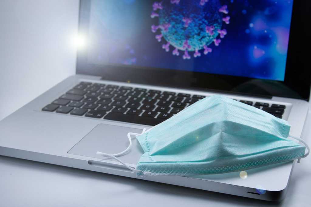A protective face mask site on a laptop displaying models of viral cells.