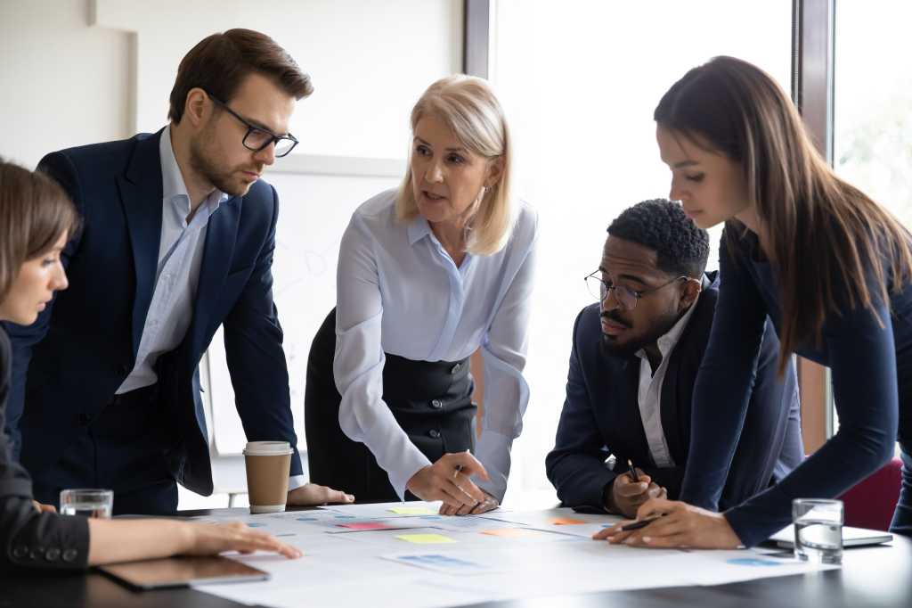 Concentrated diverse businesspeople talk brainstorm at team meeting discussing paperwork together. Focused multiracial colleagues analyze financial documents at briefing in office. Teamwork concept.