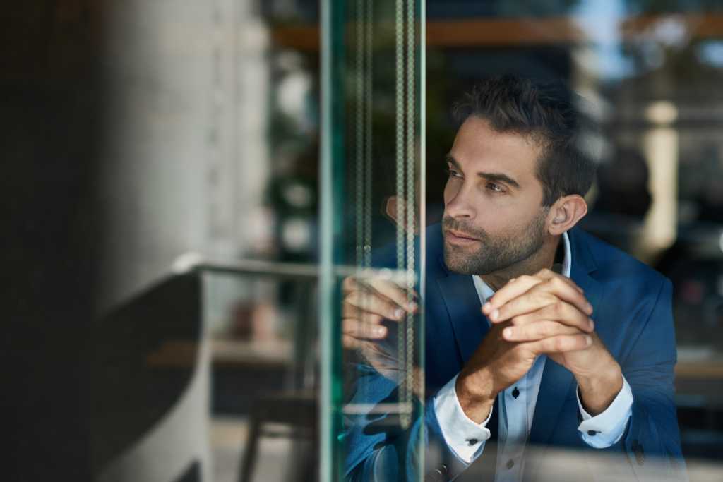 Young businessman sitting with his hands clasped at a counter by a window inside of a cafe