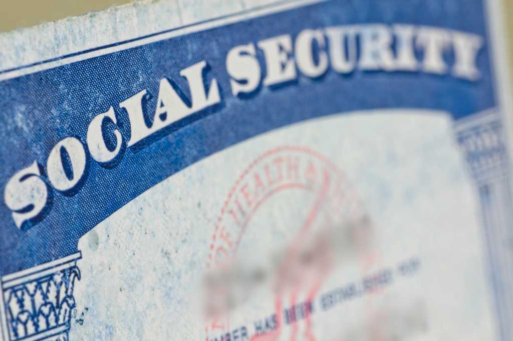 Old social security card on yellow straw table.