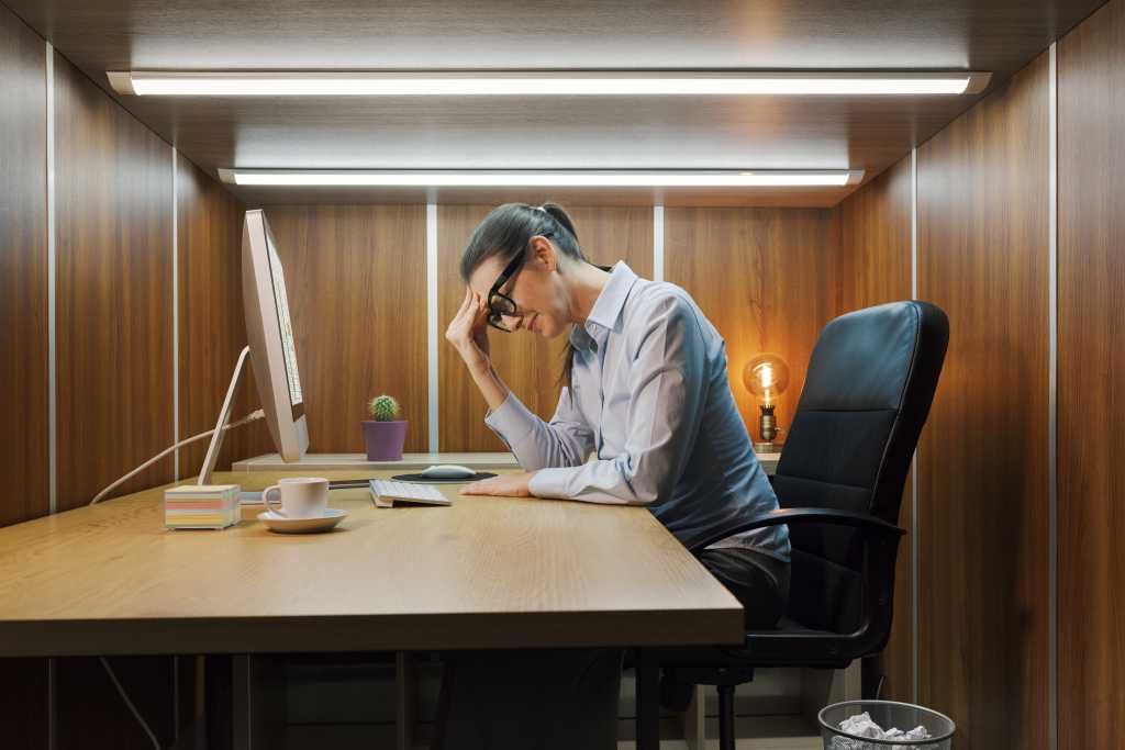 Depressed businesswoman sitting at her desk in a small boring office, she is crying and feeling hopeless