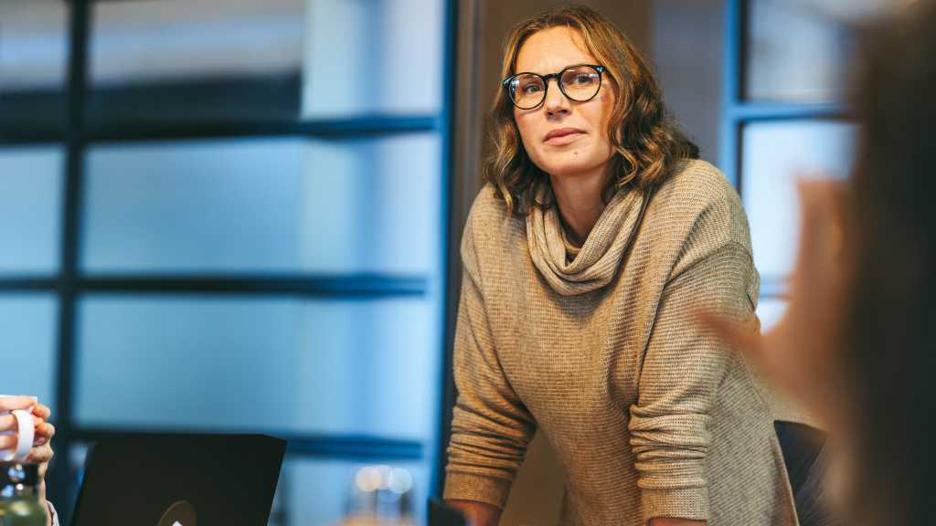 Businesswoman addresses colleagues in a boardroom. They engage in a creative discussion, promoting collaboration and teamwork. The mature leader fosters a tech-centric, startup atmosphere.