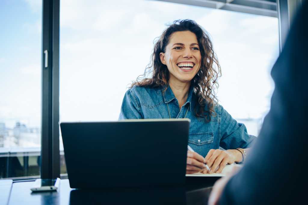 Businesswoman taking interview of a job applicant in office boardroom. Smiling recruiter asking questions to a male candidate during job interview.