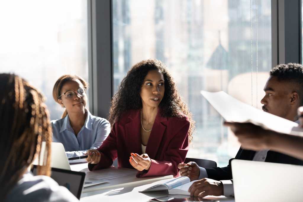 Concentrated young african american female leader boss negotiating business ideas or developing project growth ideas with motivated mixed race employees workers managers at brainstorming meeting.