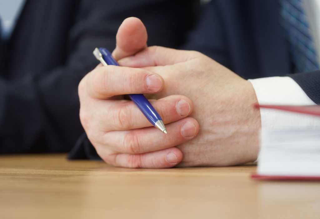 Folded hands of politician, deputy or businessman on the table along with pen. Official, boss, lawyer or delegate. Participation in negotiations. Copy space. No face. Close-up