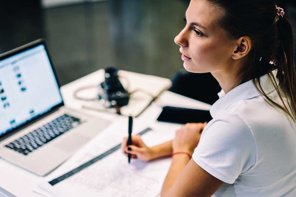 Selective focus on female architect looking away thinking about accountings while drafting at desktop with laptop computer, skilled young woman pondering on doing homework sketch for design courses