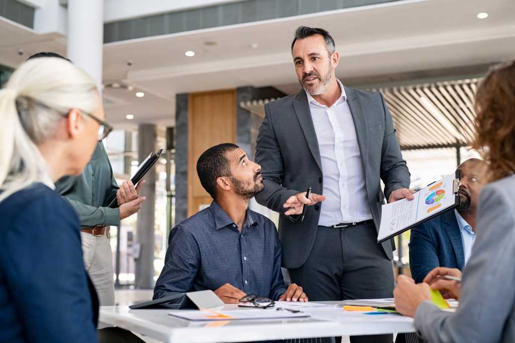 Successful entrepreneur focusing on work with charts during meeting with multiethnic employee. Mature businessman discussing work at conference table in office with senior businesswoman.