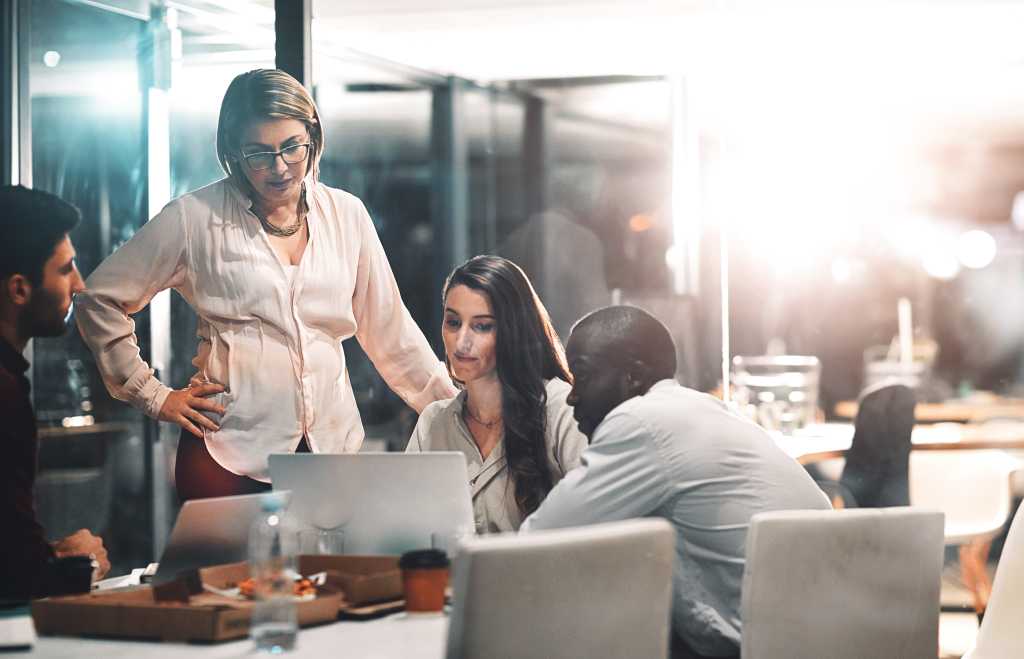 Night, management and business people with laptop in meeting for creative project, deadline and review. Web design, employees and team with mentor in office for ux information, feedback and overtime