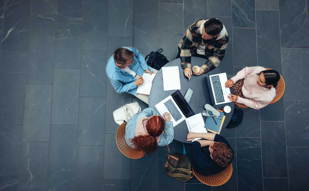 Top view of group of students sitting together at table. University students doing group study.